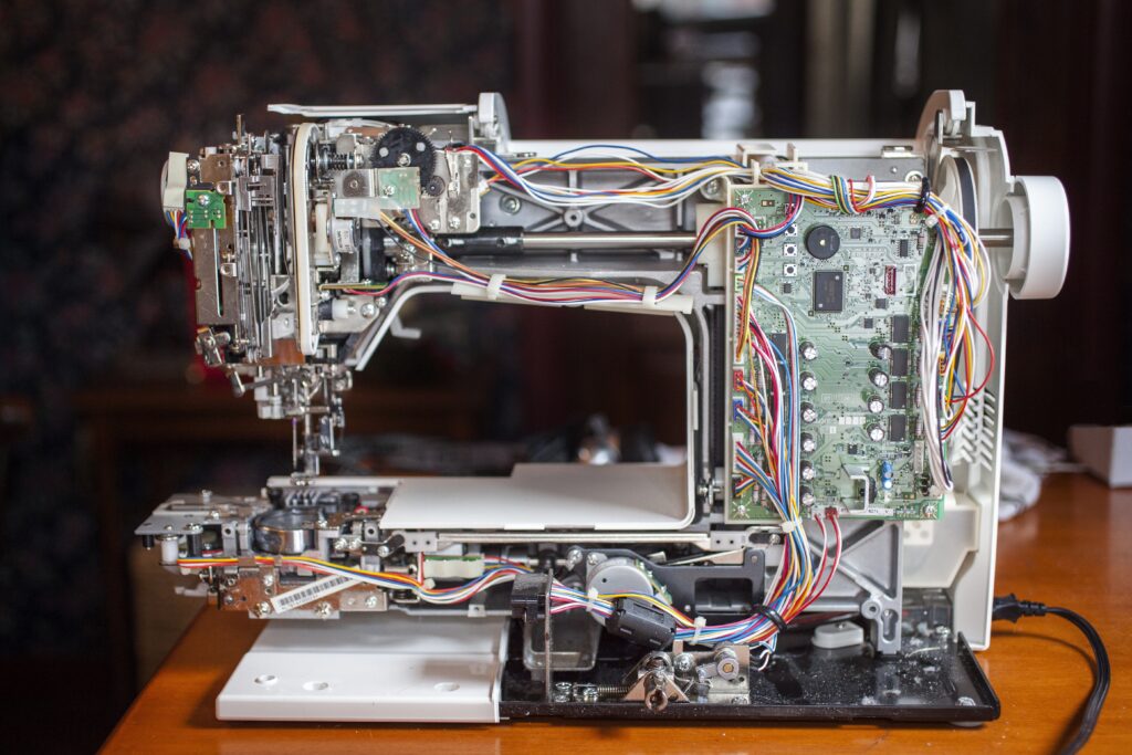 the inside view of a sewing machine with wires and motherboard exposed.
